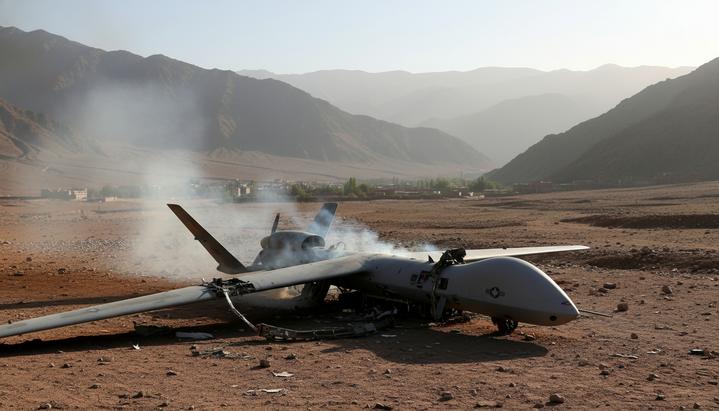 Обломки сбитого американского беспилотника MQ-9 Reaper, дымящиеся в скалистой засушливой долине в горах Афганистана.