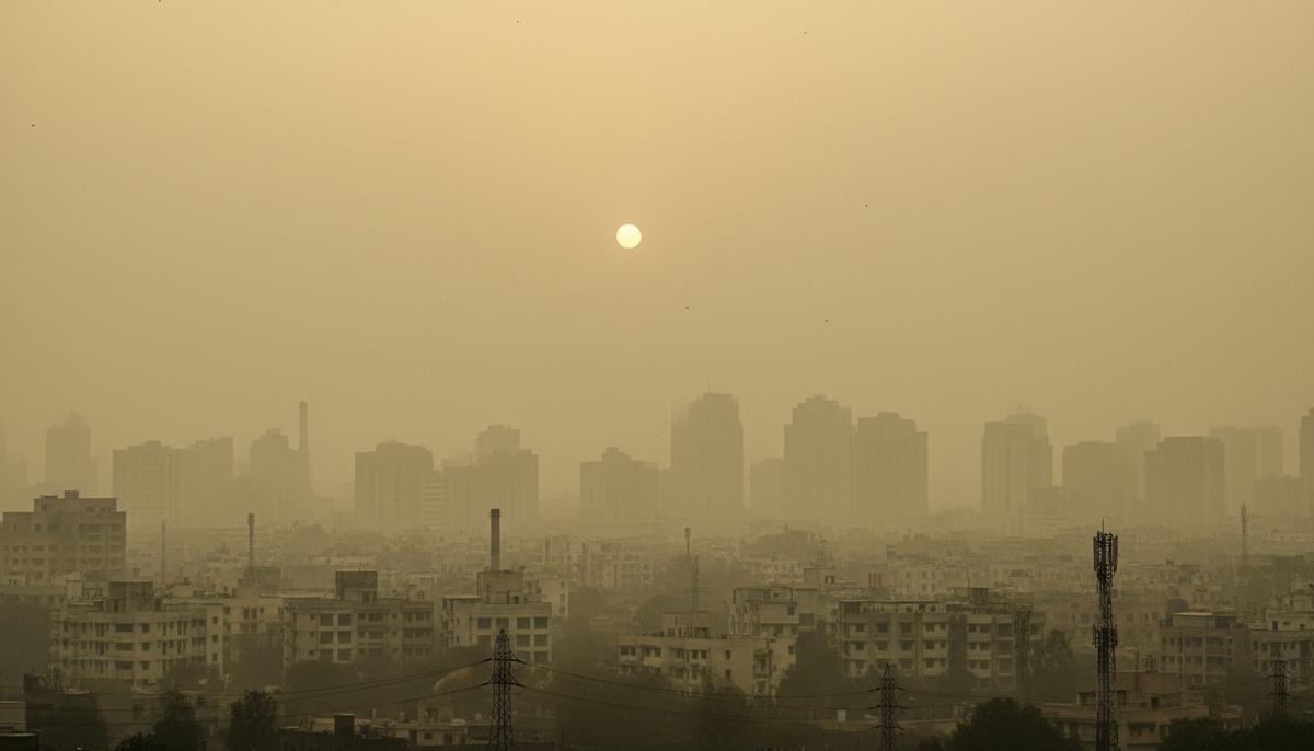 Густой желто-коричневый смог, скрывающий силуэты зданий крупного азиатского города на рассвете.